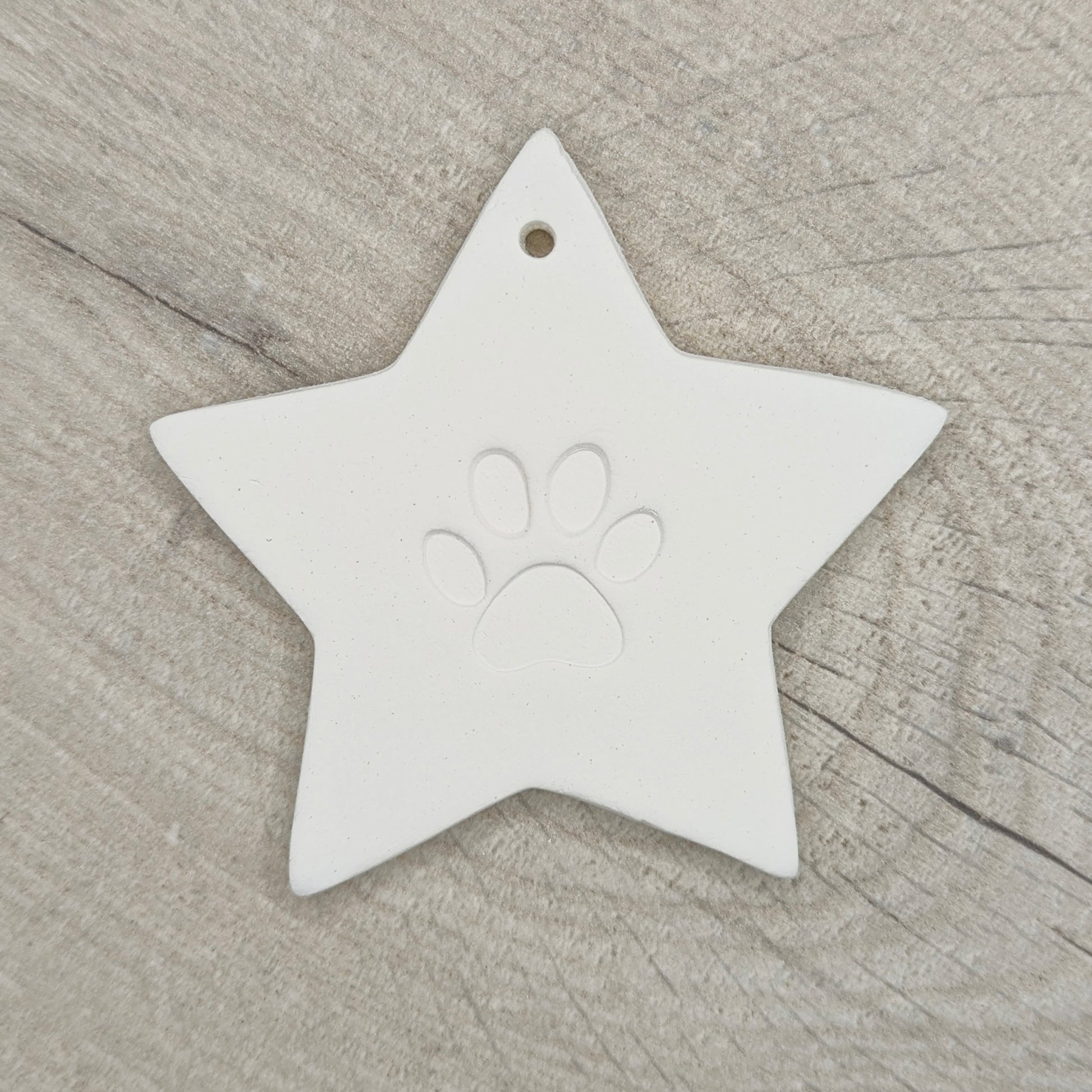 Star shaped clay decoration with a paw print design in the centre on a wooden surface