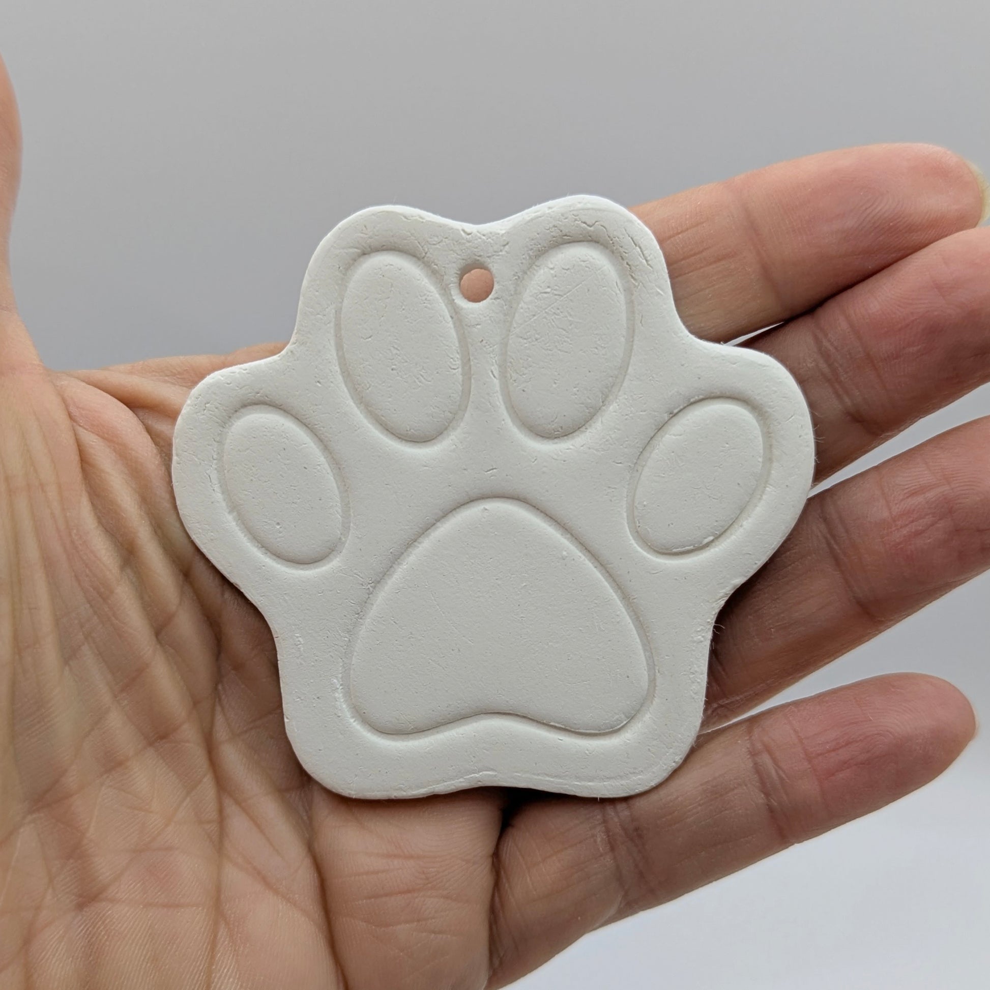 White paw print clay decoration held in a hand against a gray background