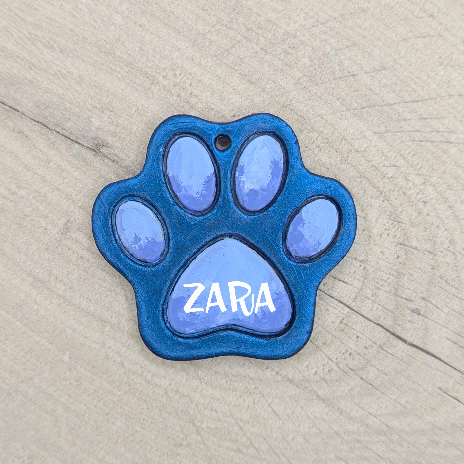 Blue painted paw-shaped clay decoration with 'ZARA' painted onto it