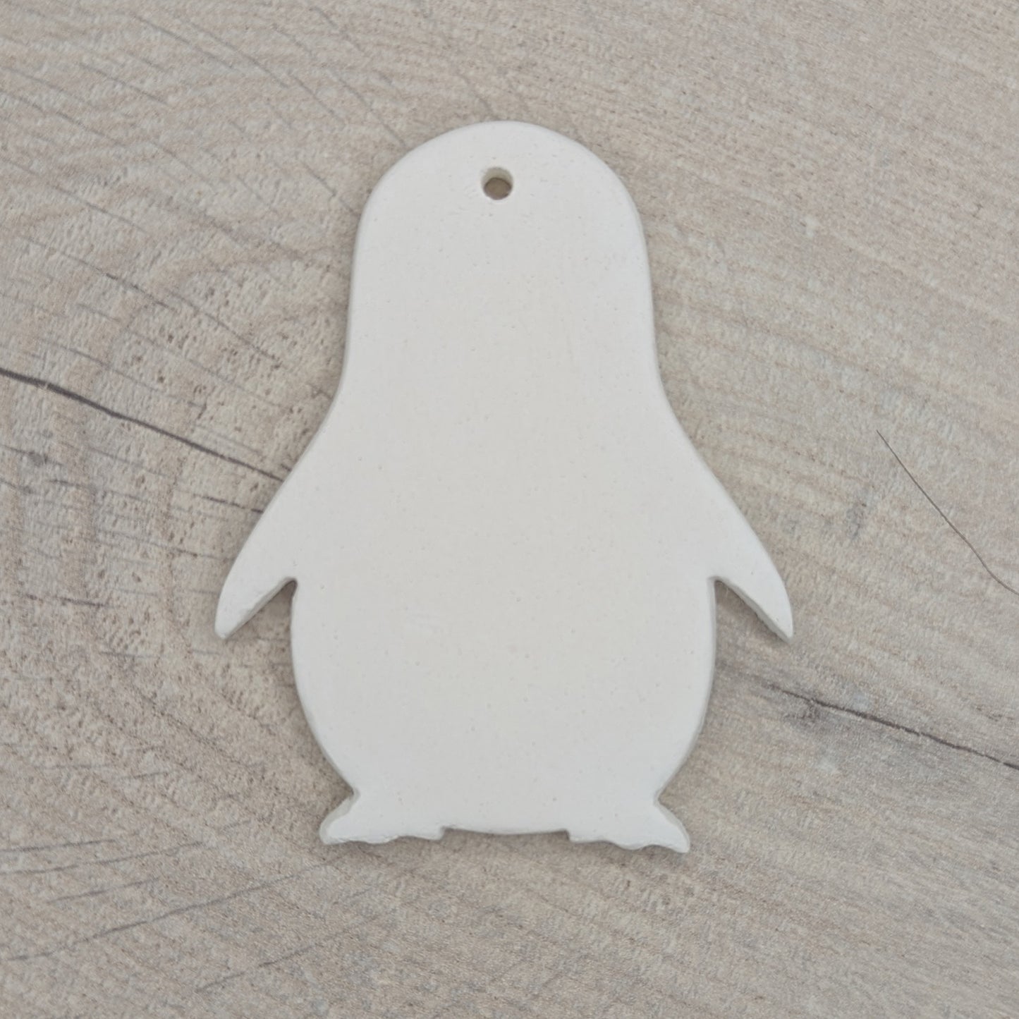 White penguin-shaped clay ornament on a wooden surface