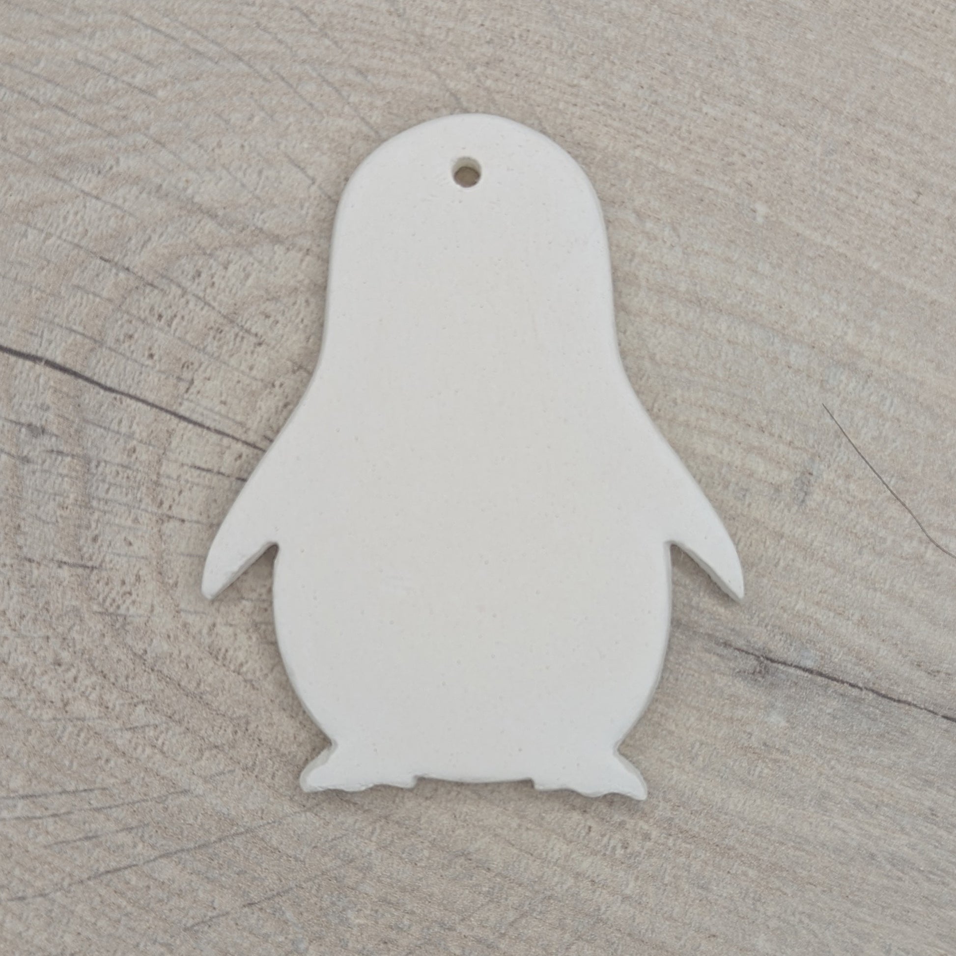 White penguin-shaped clay ornament on a wooden surface
