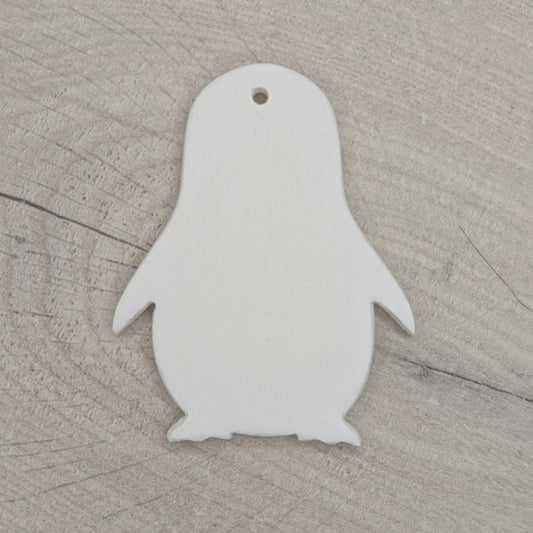White penguin-shaped clay ornament on a wooden surface