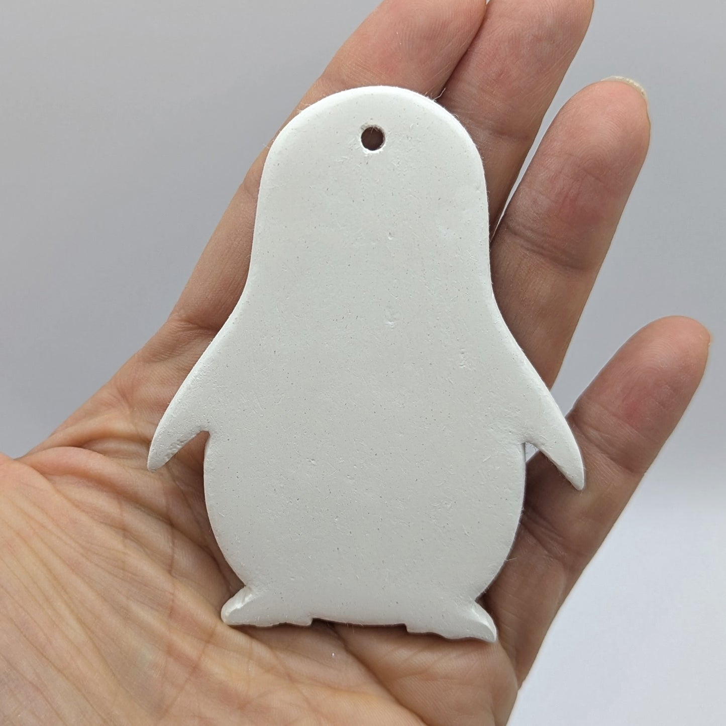 White penguin shaped clay ornament held in a hand paint and decorate at home