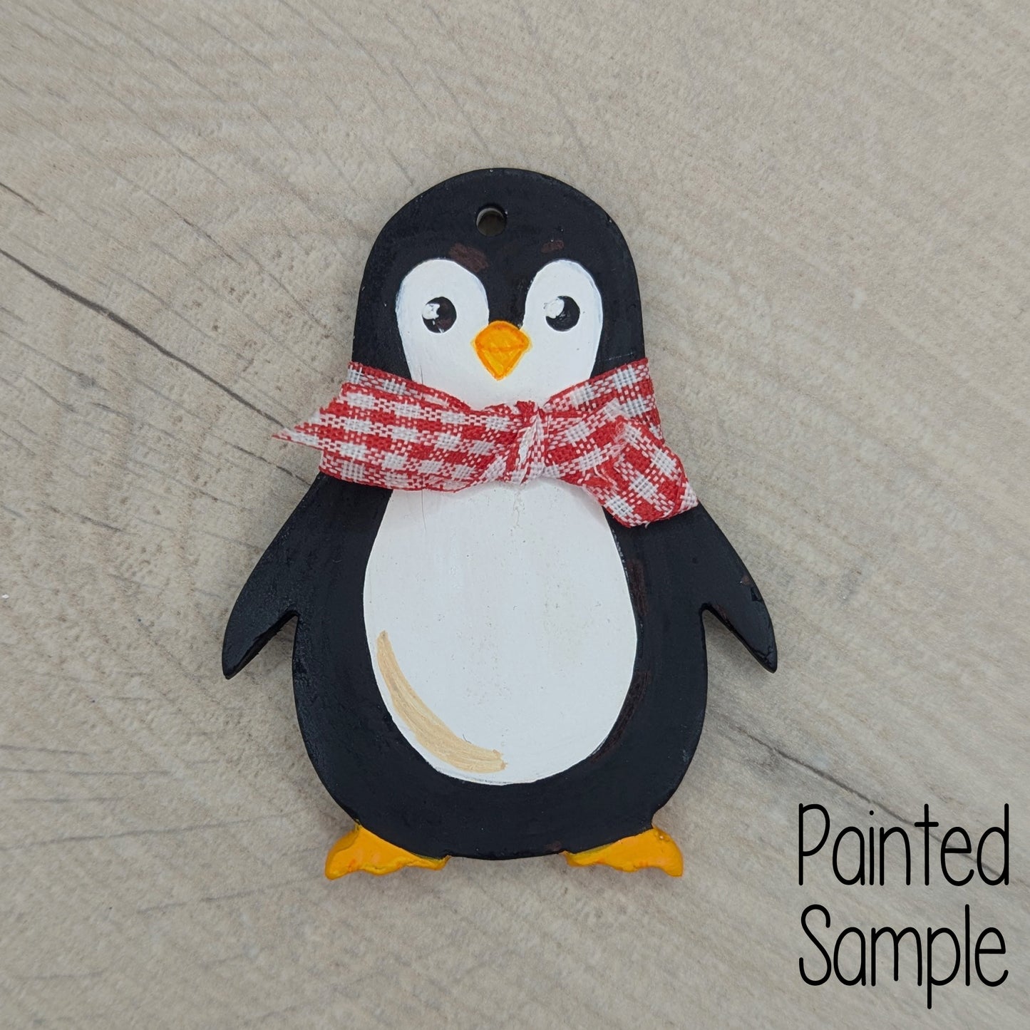 festive penguin clay sample decoration, painted in traditional black and white penguin colours with a red and white gingham ribbon round the neck