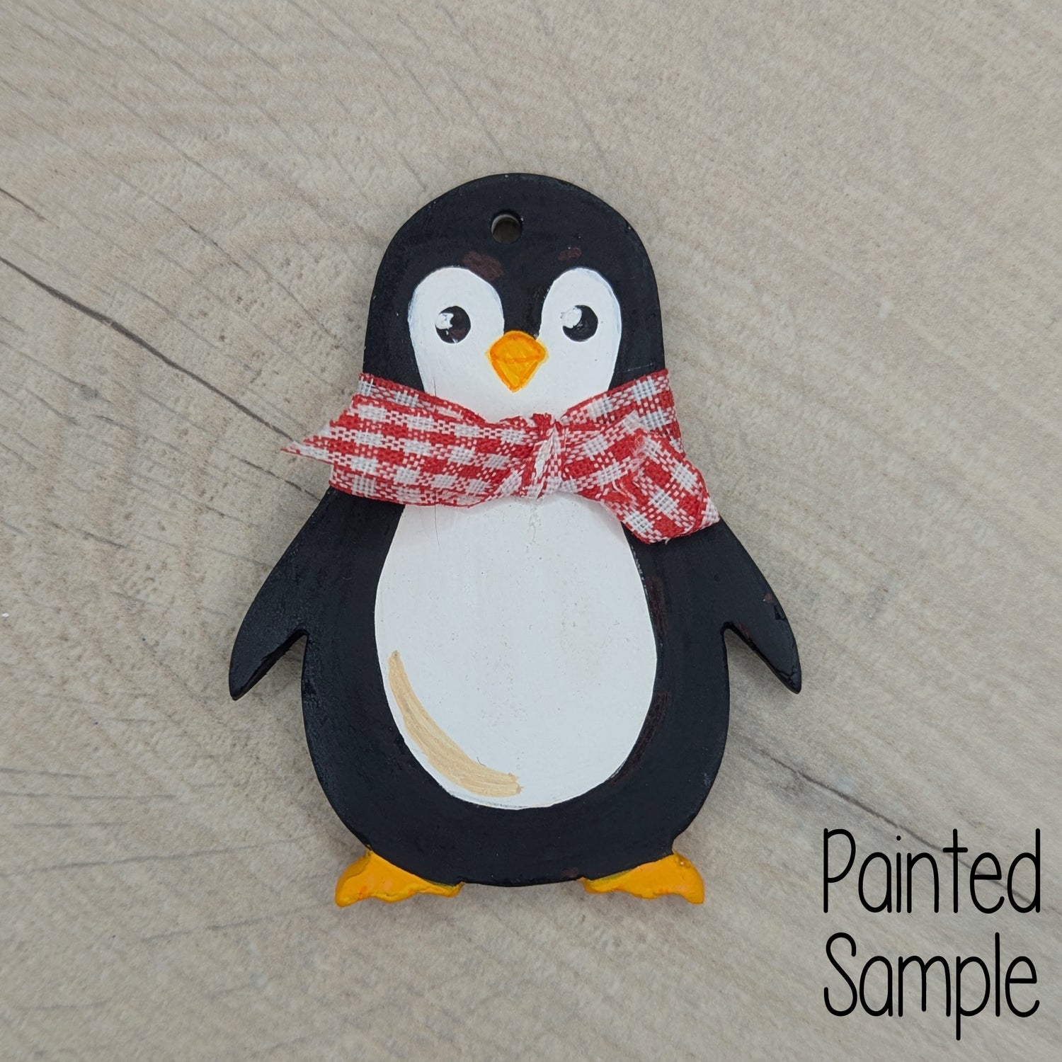 festive penguin clay sample decoration, painted in traditional black and white penguin colours with a red and white gingham ribbon round the neck