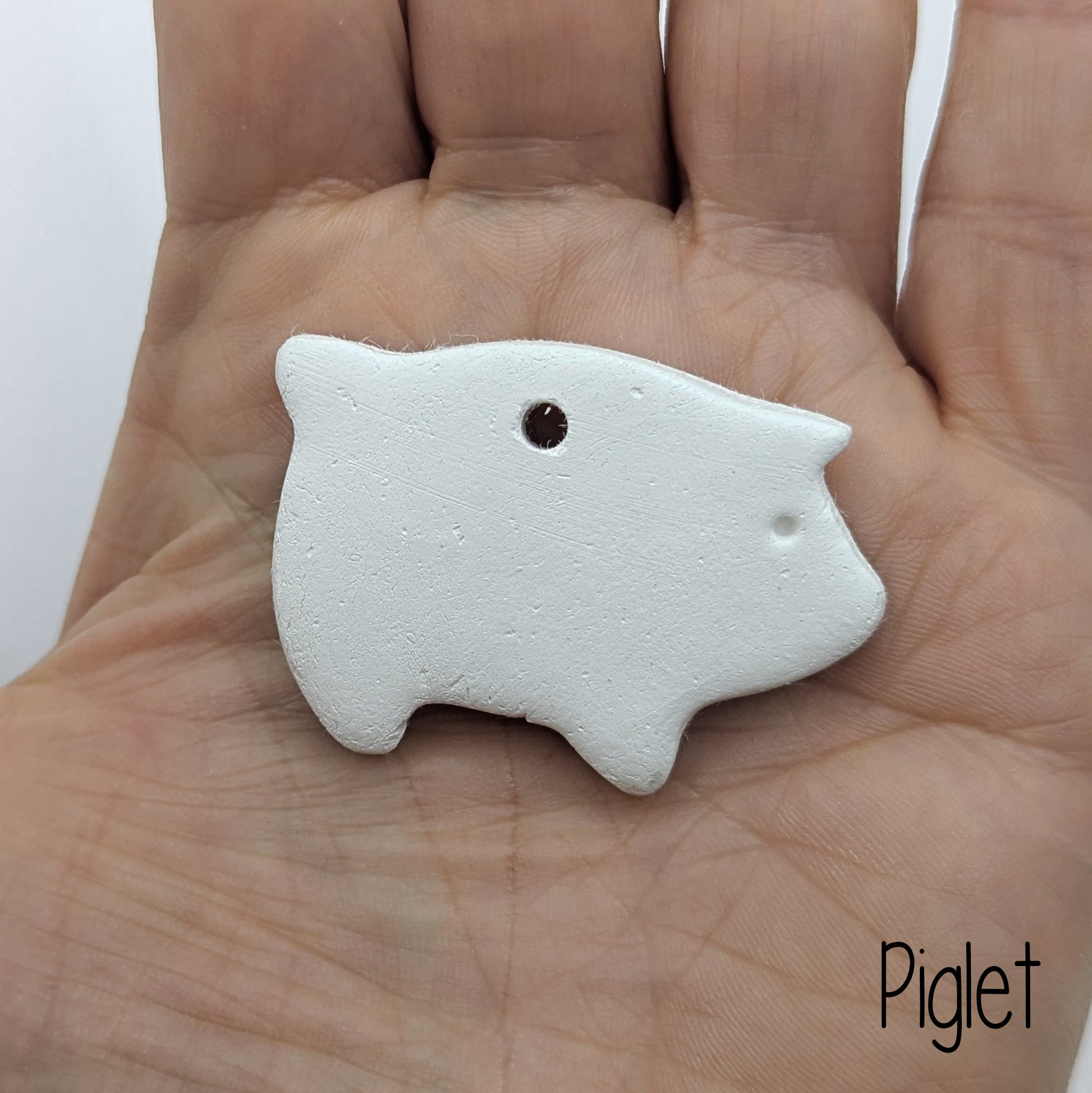 air dried clay decoration in the shape of a piglet, shown in hand for scale