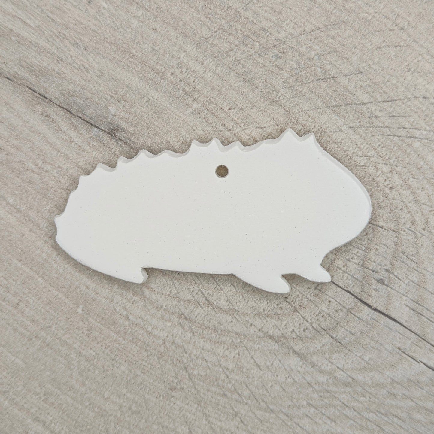 white rough furred guinea pig shaped decoration made out of air dried clay shown on a light wood background