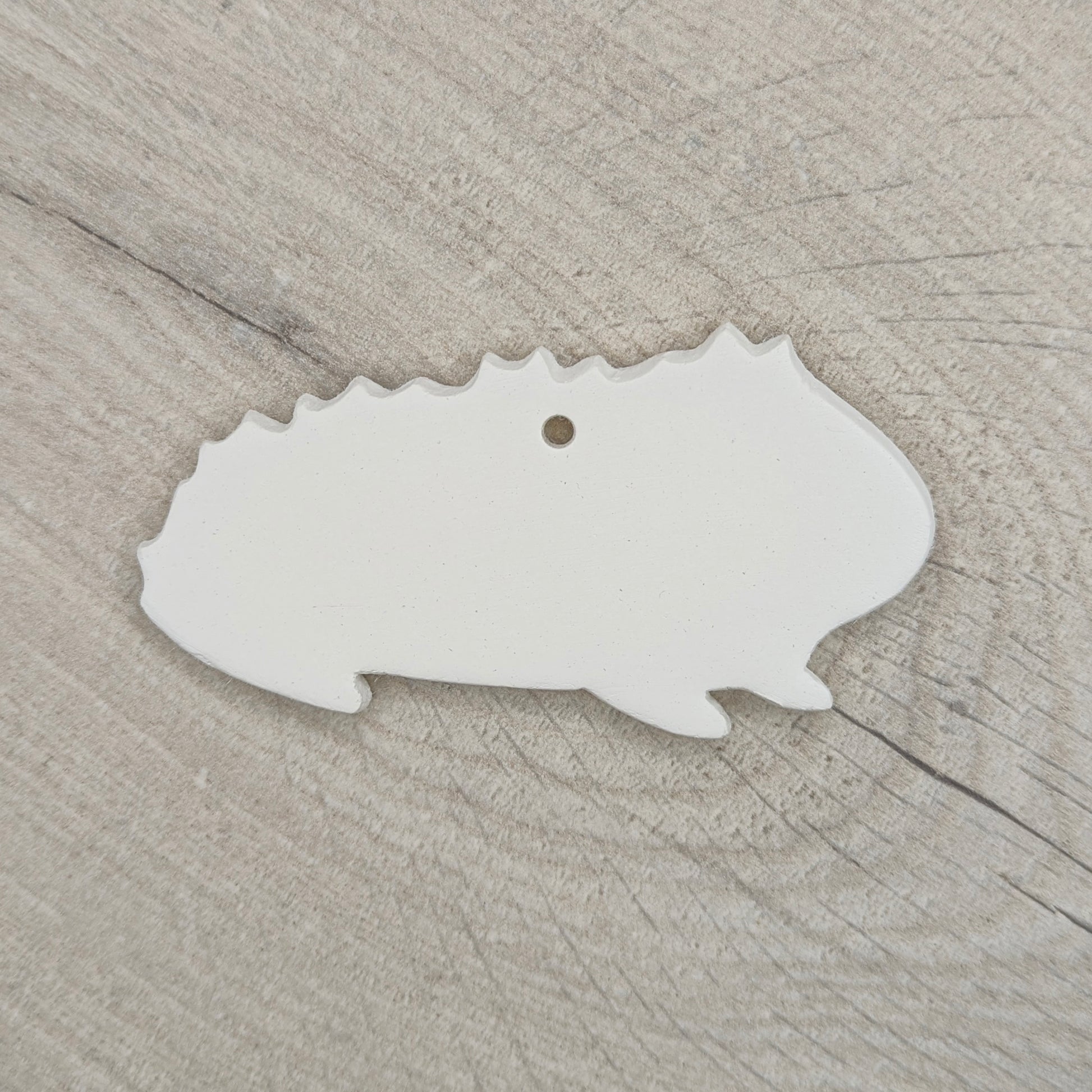 white rough furred guinea pig shaped decoration made out of air dried clay shown on a light wood background