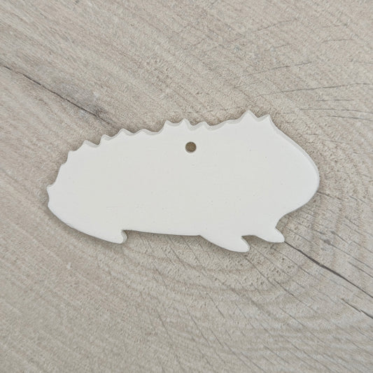 white rough furred guinea pig shaped decoration made out of air dried clay shown on a light wood background