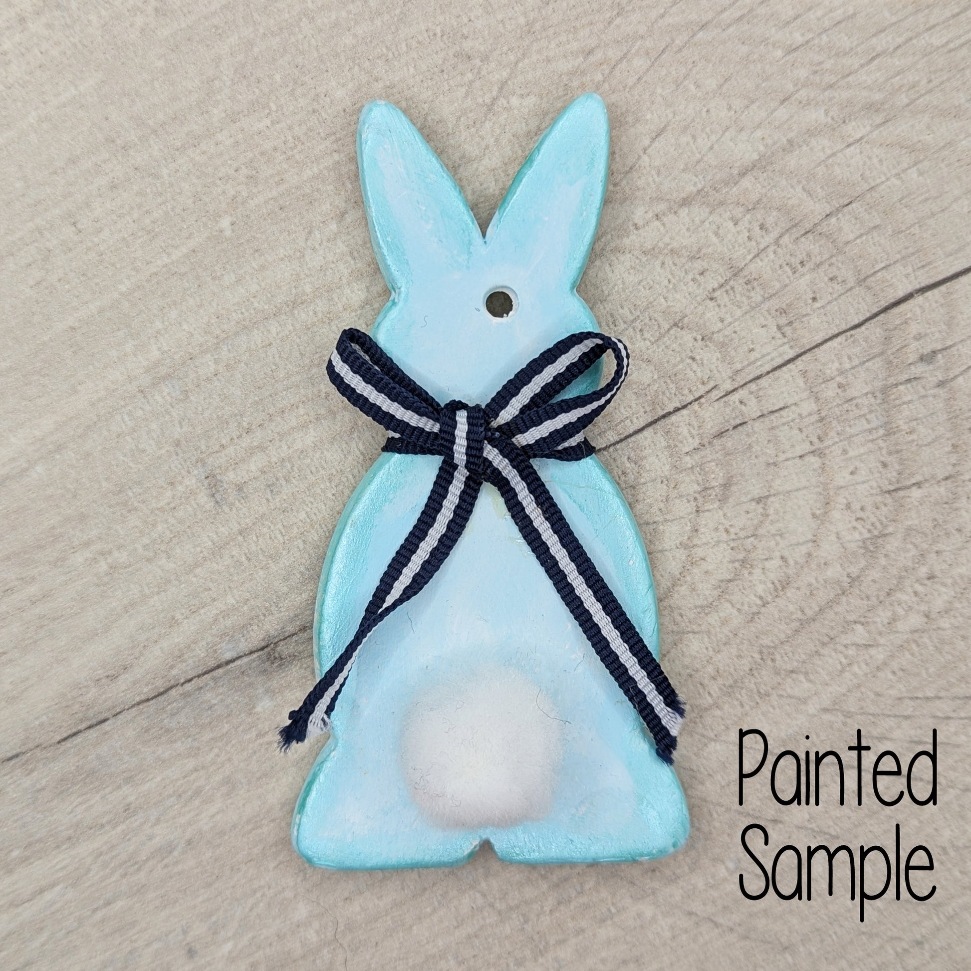 clay rabbit decoration, painted in pastel blue with a white pom pom tail and a black and white ribbon around the neck