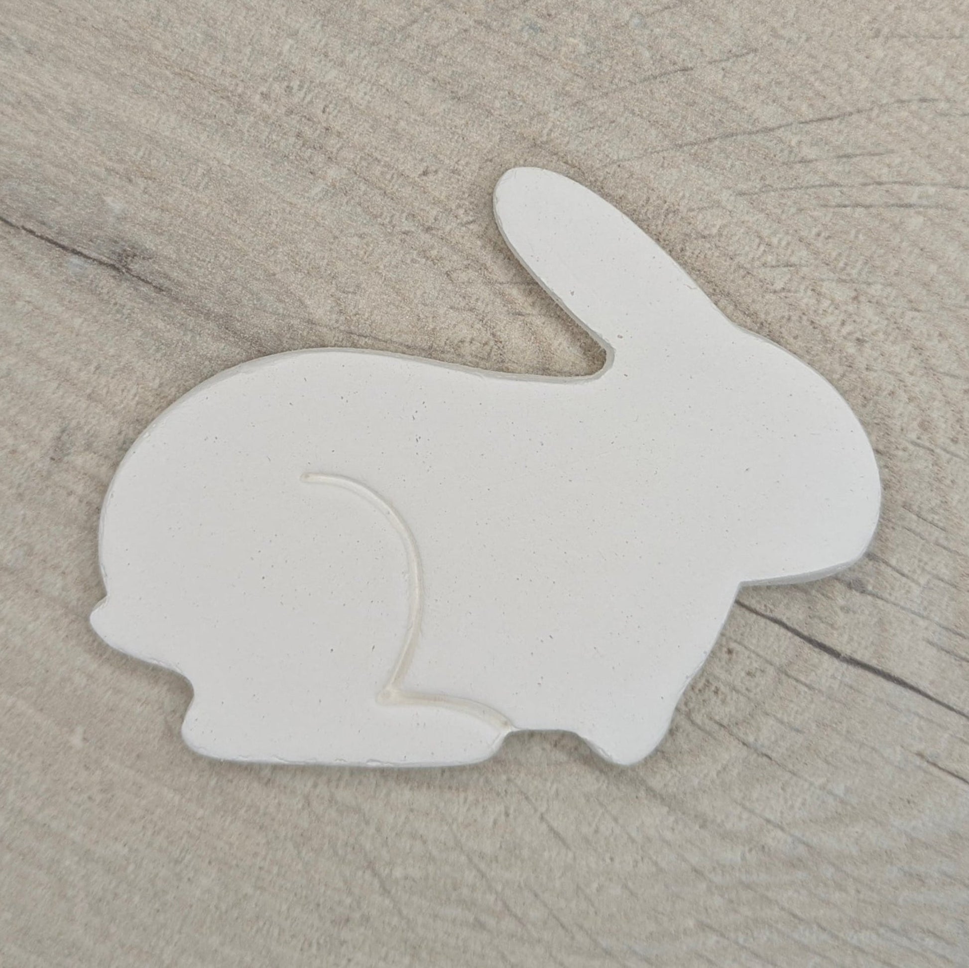 Side view of a rabbit made from air dried clay displayed on a light wooden background