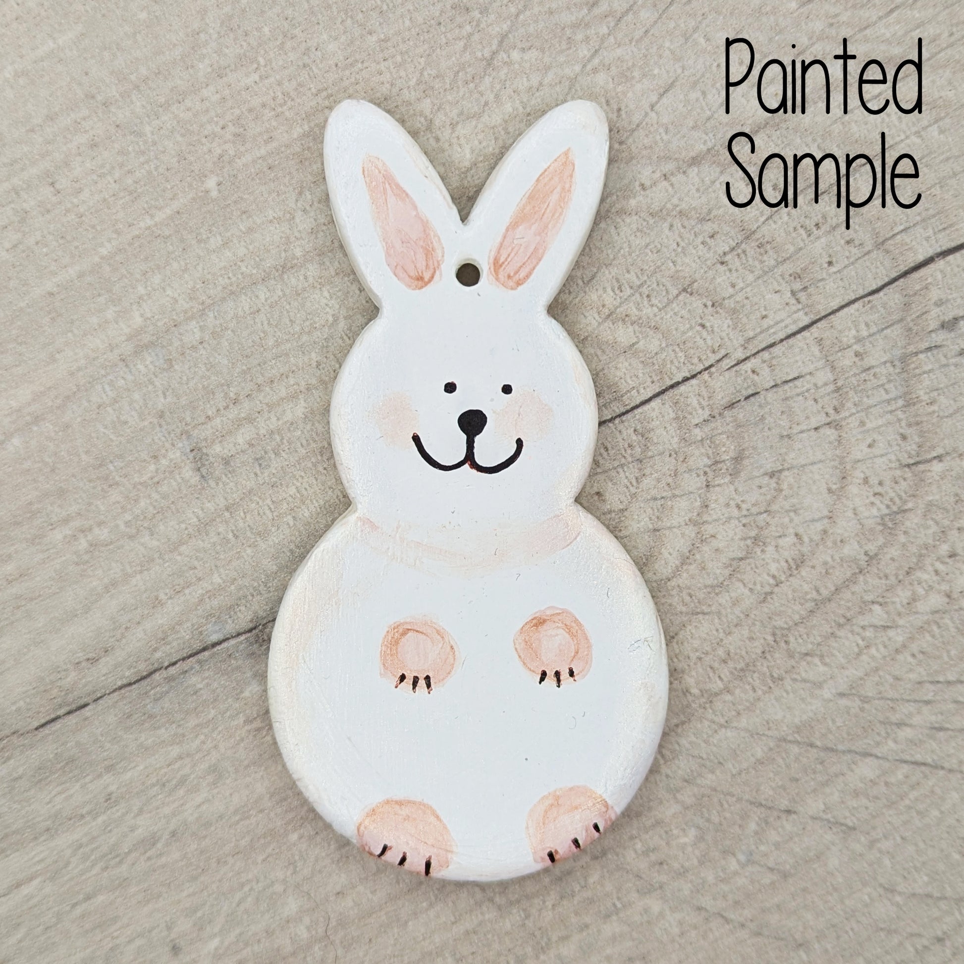 sample of a painted rabbit clay decoration, painted in off white with peach paws and a cute black smiling face