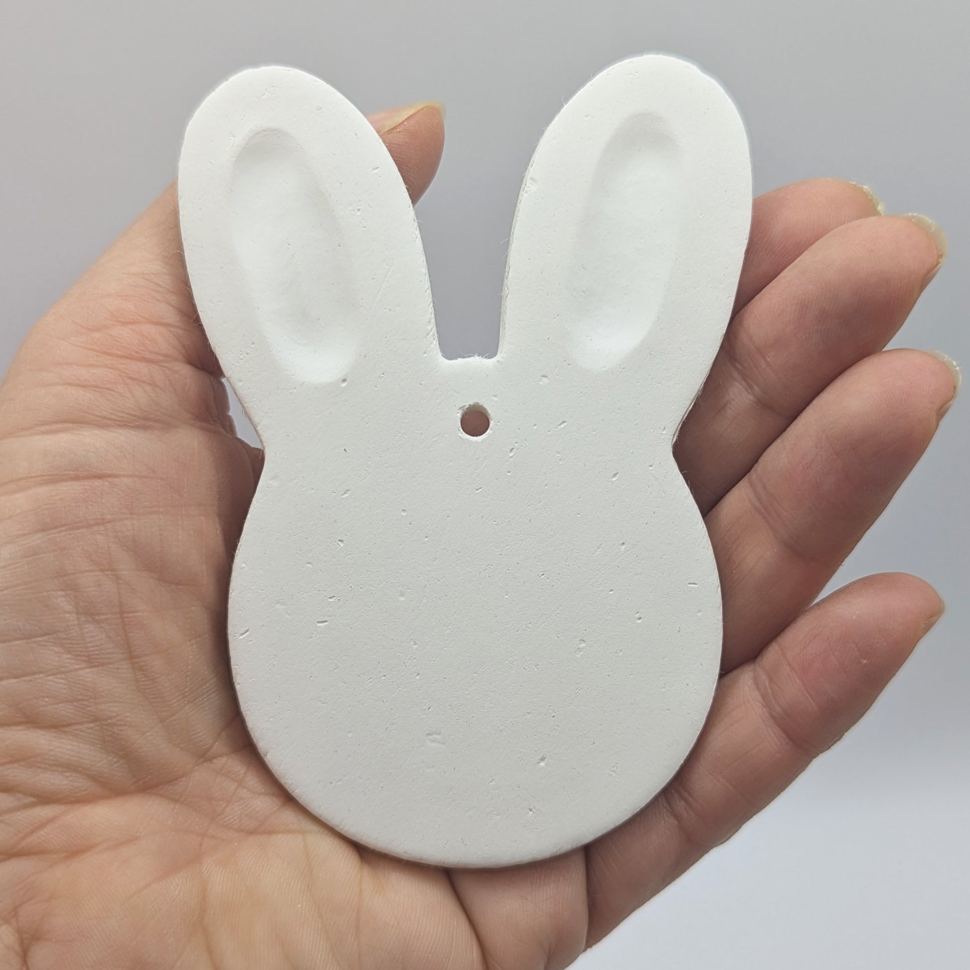 a wide rabbit head / face clay decoration in some ones hand to show scale