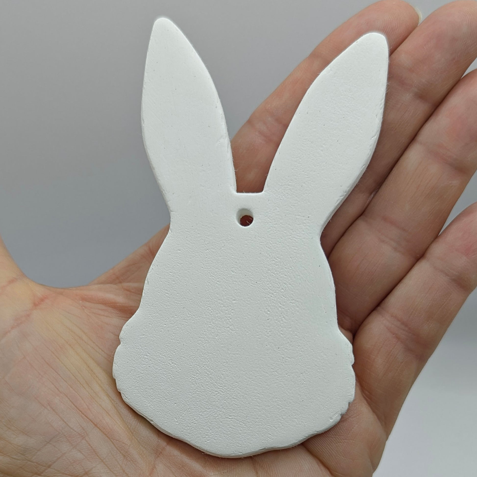 White bunny-shaped clay decoration held in a hand against a gray background
