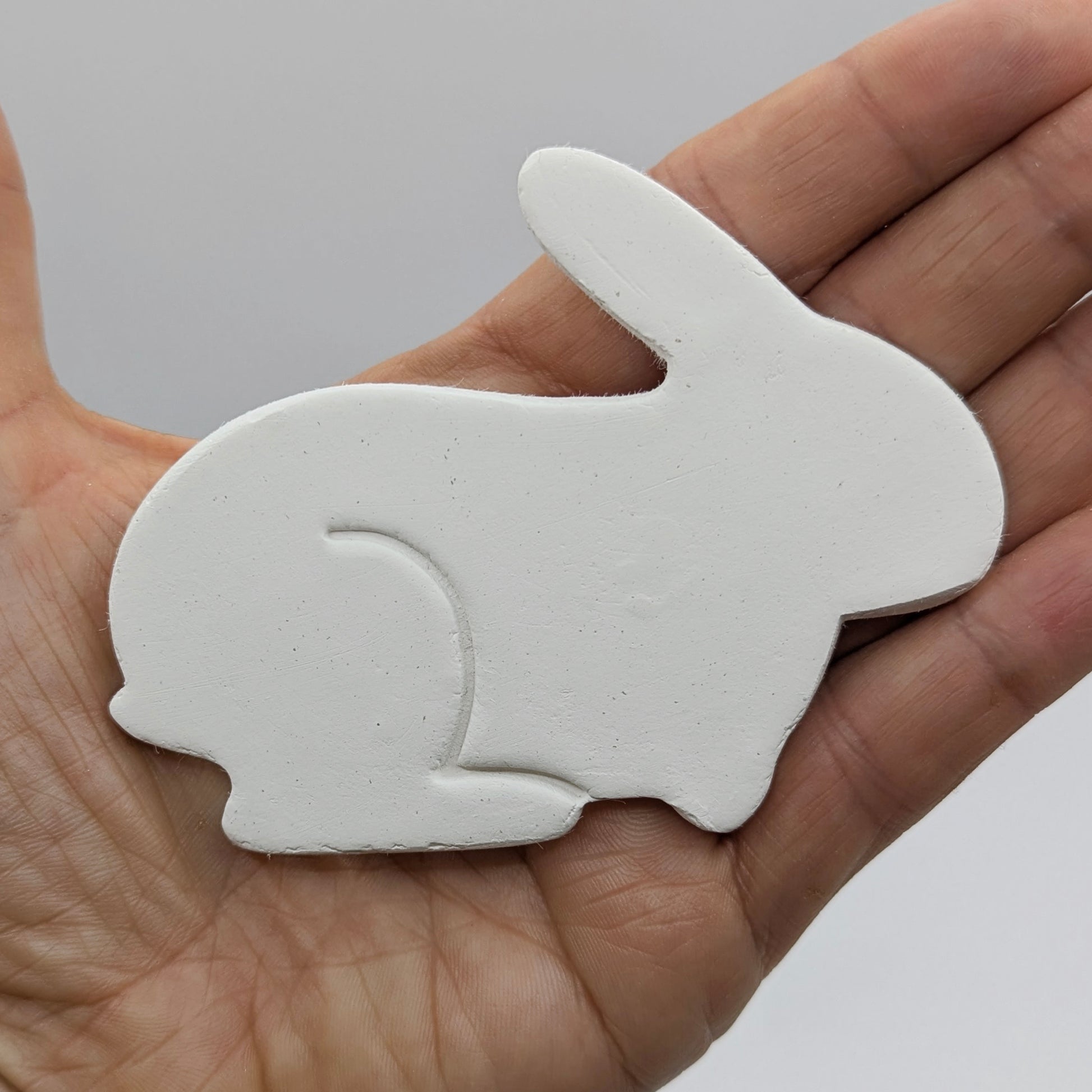 Side view of a rabbit made from air dried clay held in some ones hand to show scale