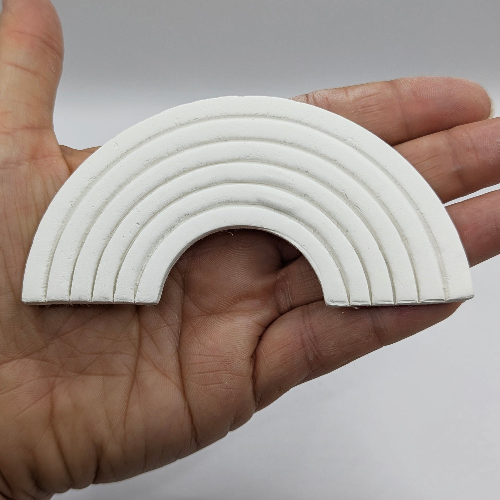 white clay rainbow in some ones hand to show scale