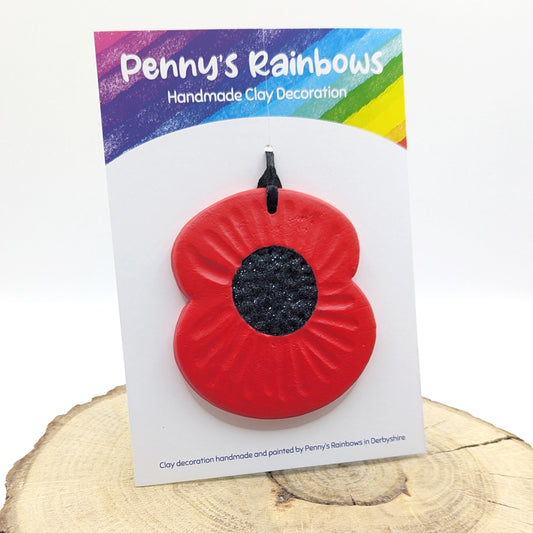 handmade clay poppy decoration, painted in red and black and displayed on a penny's rainbows backing card