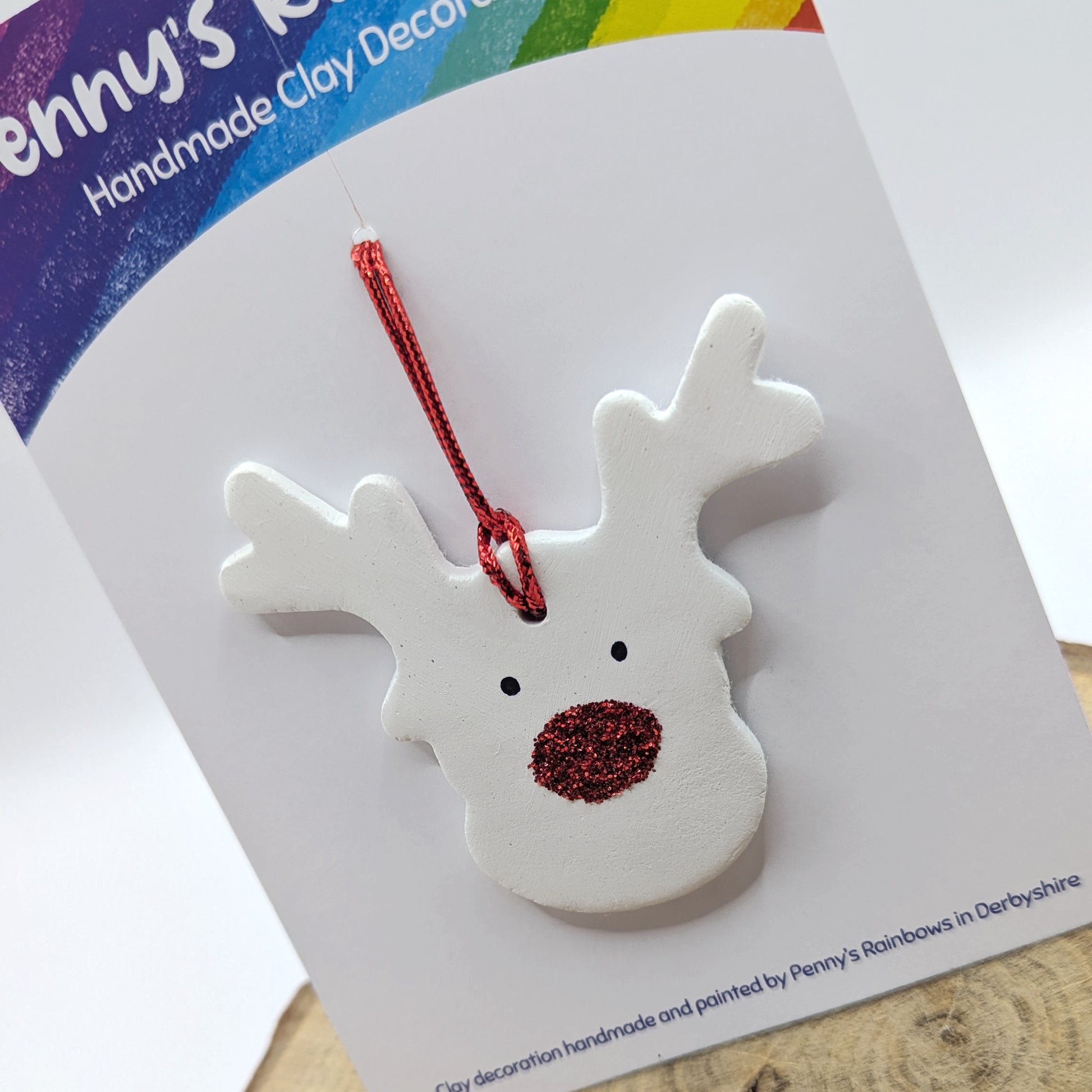 White clay reindeer ornament with red nose and antlers on a card with 'Penny's Rainbows' branding.