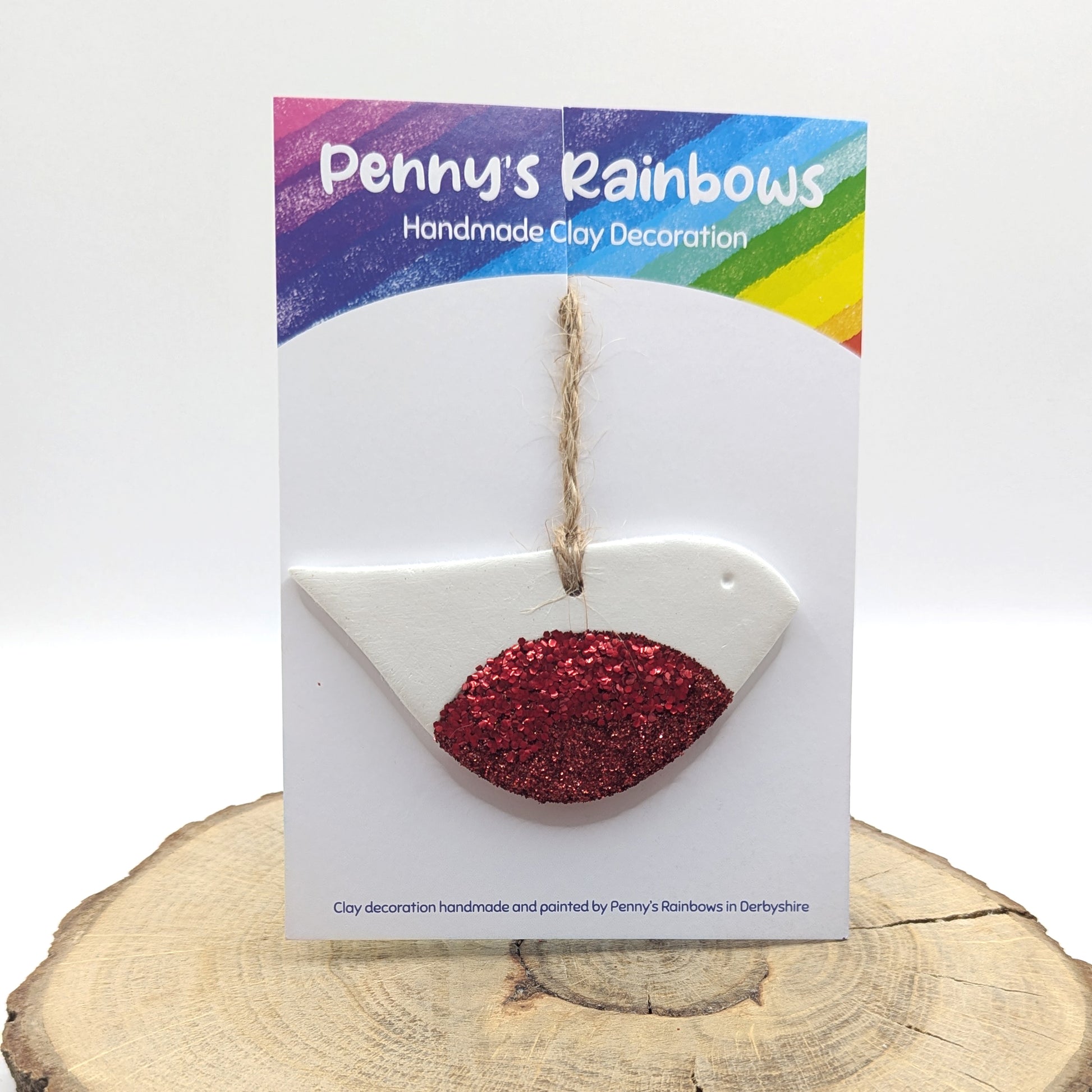 Handmade clay decoration in the shape of a stylised robin with red glitter on chest, on a 'Penny's Rainbows' branded card