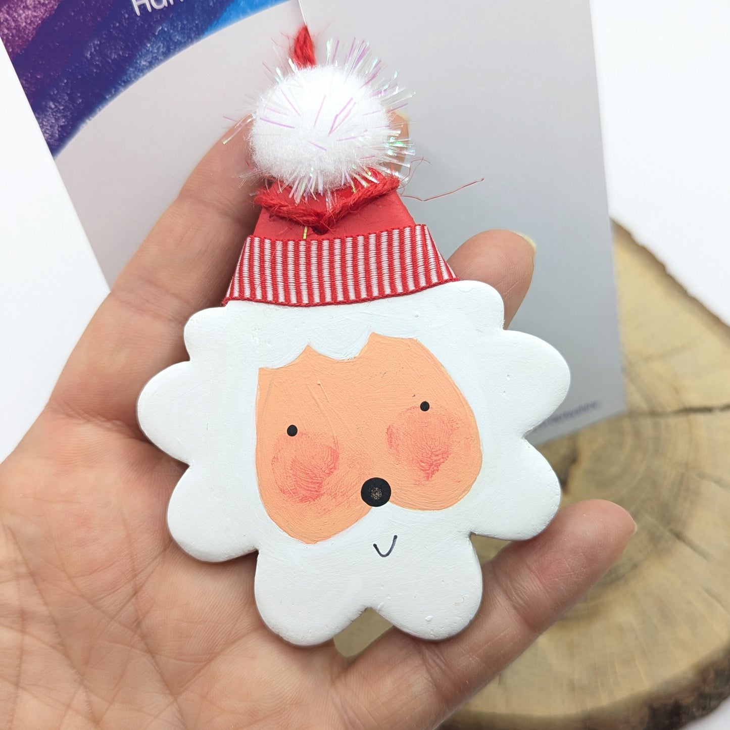 painted santa clay decoration , with ribbon and white pom pom on hat top, held in hand
