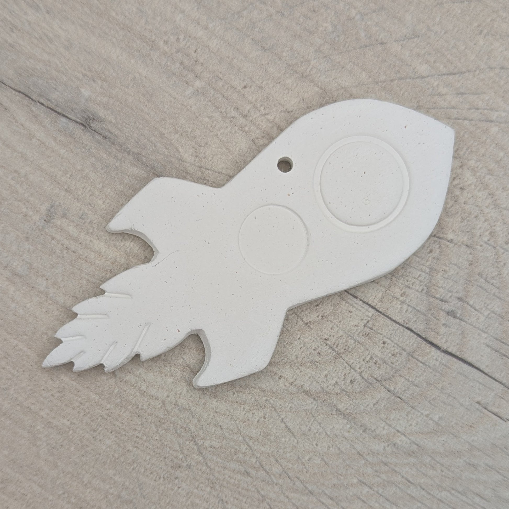 air dried clay decoration in the shape of a rocket, on a wooden surface