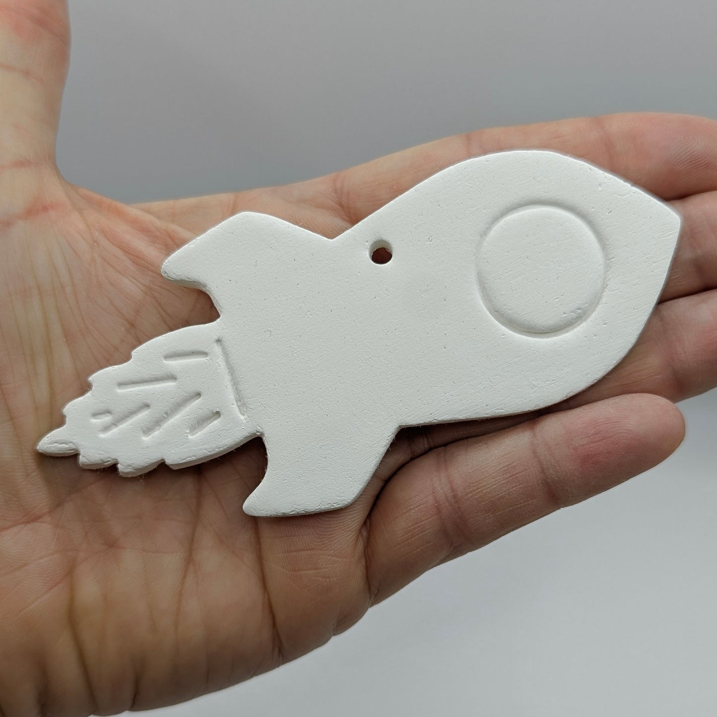 White ceramic rocket-shaped ornament held in a hand against a gray background