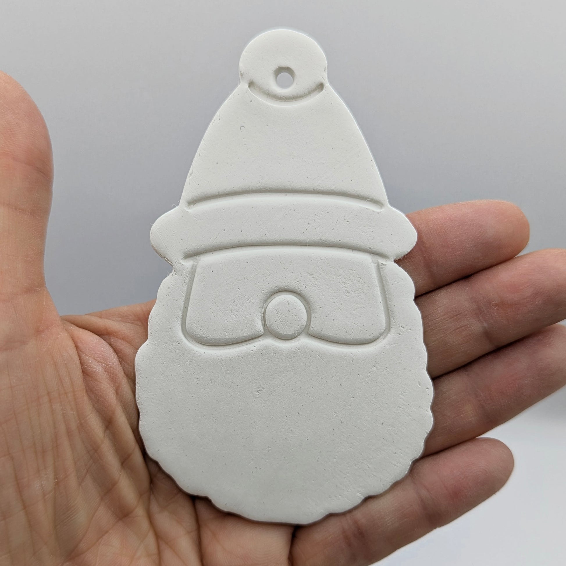 a clay decoration in the shape of santa claus's head and hat held in some ones hand for scale