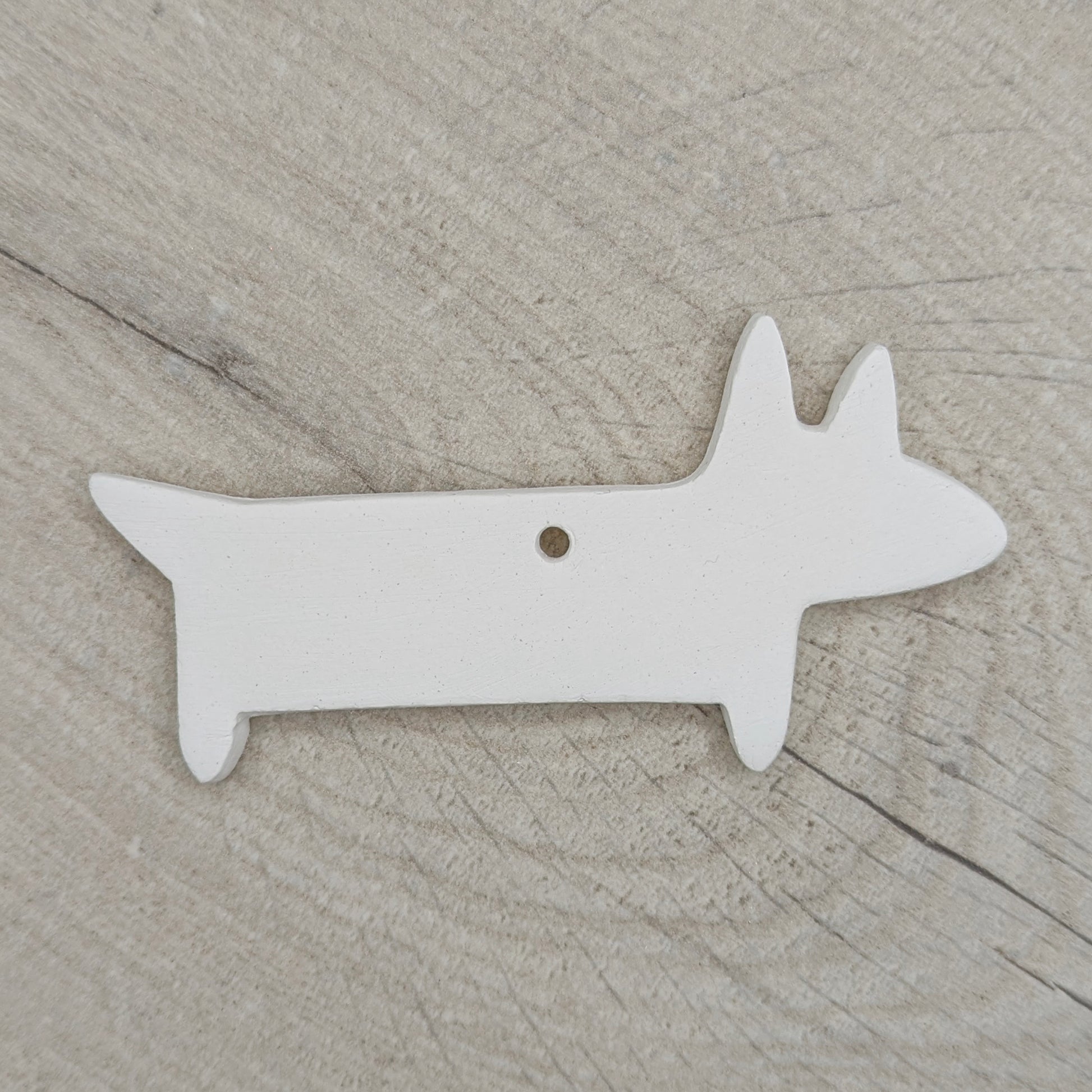 white clay decoration in the shape of a sausage dog on a wooden background