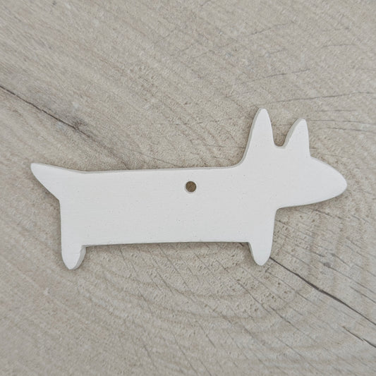 white clay decoration in the shape of a sausage dog on a wooden background