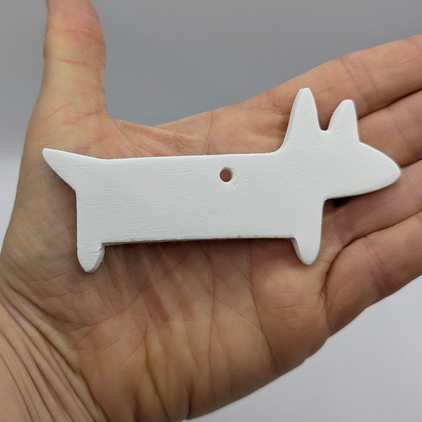 white clay sausage dog decoration shown in a hand for size