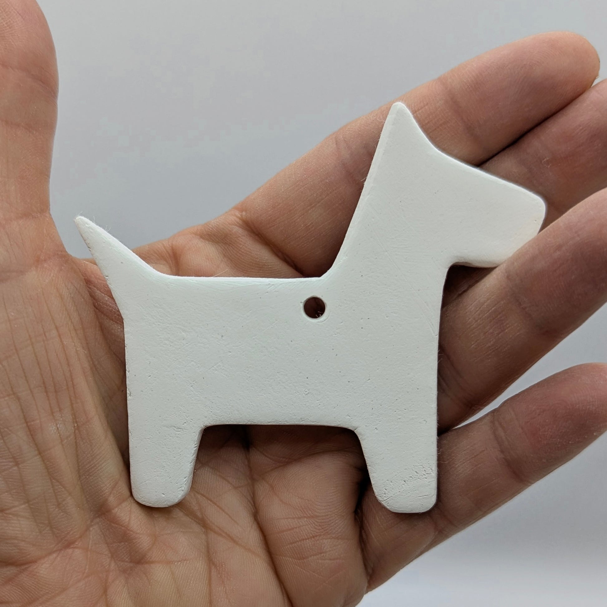 white air dried clay decoration in the shape of a scotty dog, shown in some ones hand for scale