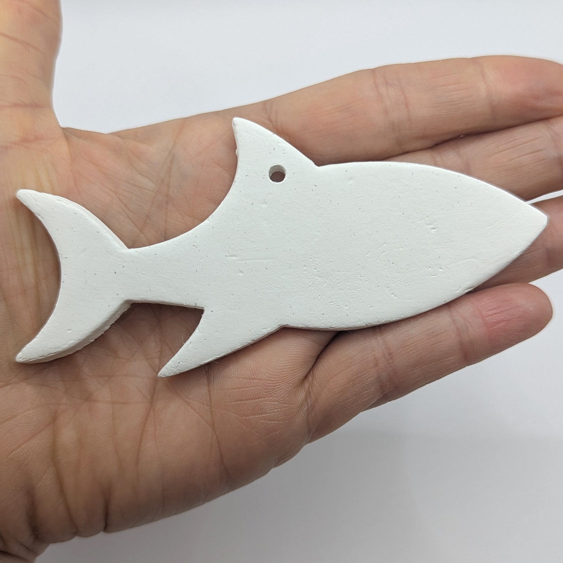white air dried clayed decoration in the shape of a shark, held in hand to show scale