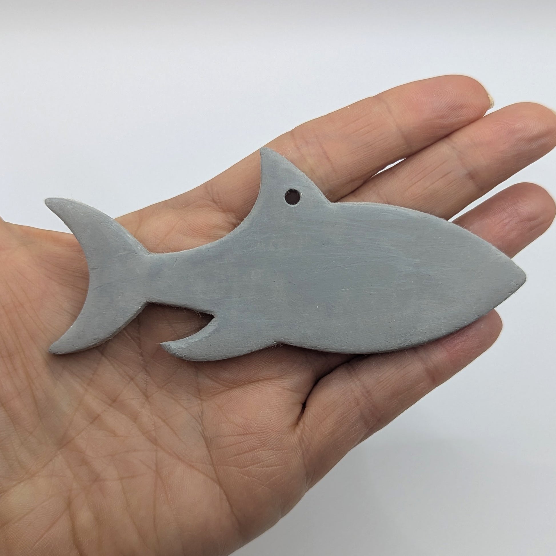 grey air dried clayed decoration in the shape of a shark, held in hand to show scale