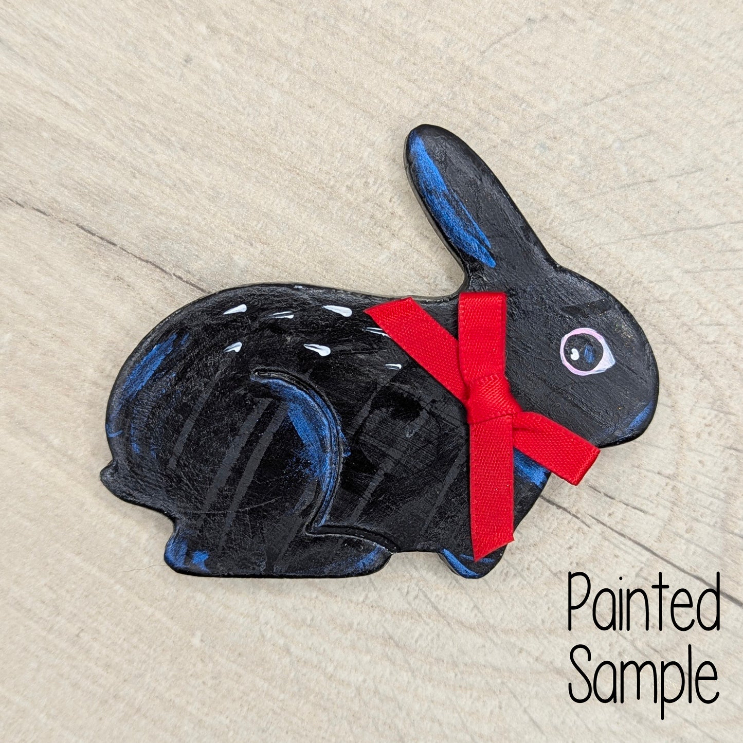 Painted black rabbit with a red bow on a light wood surface, labeled 'Painted Sample'.