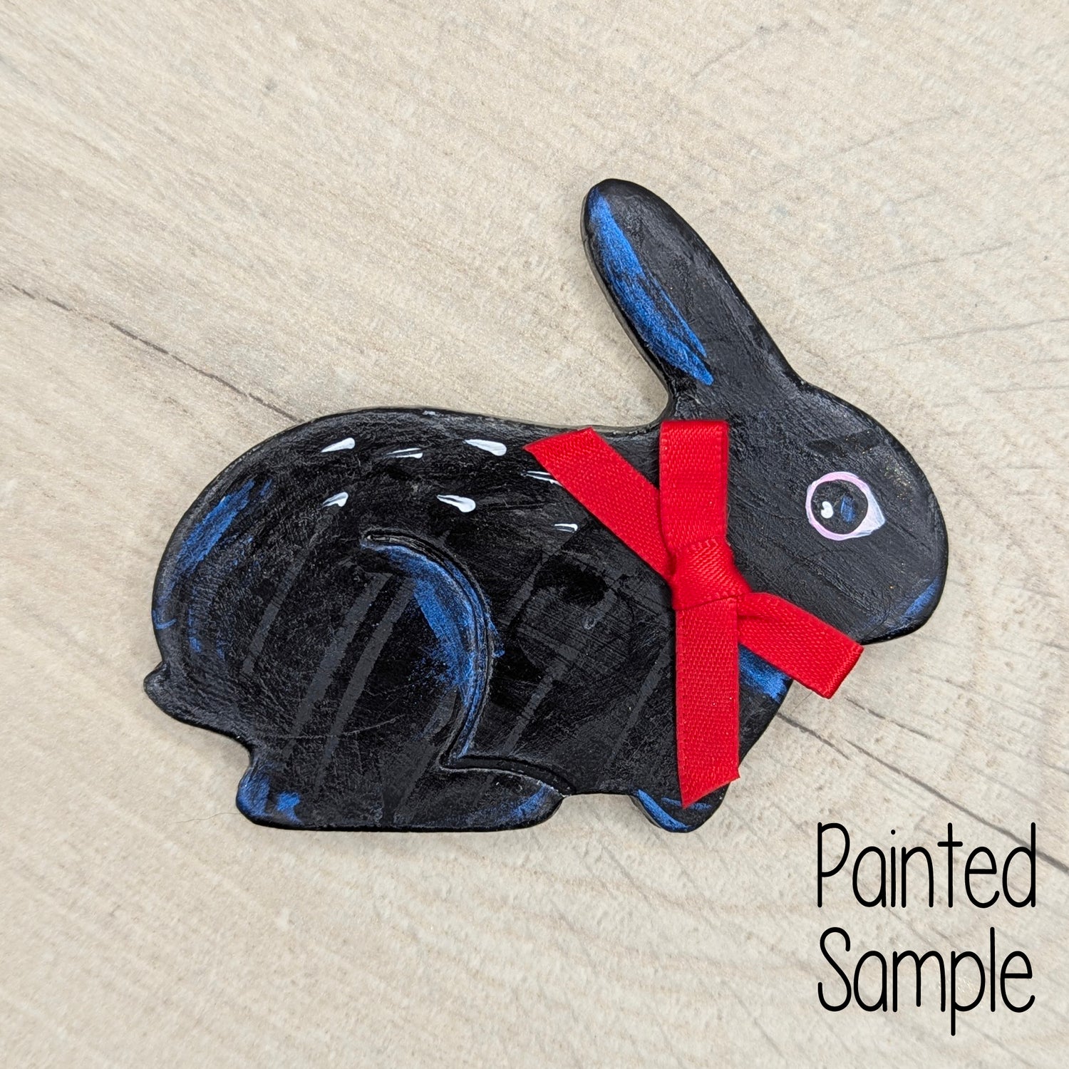 Painted black rabbit with a red bow on a light wood surface, labeled 'Painted Sample'.