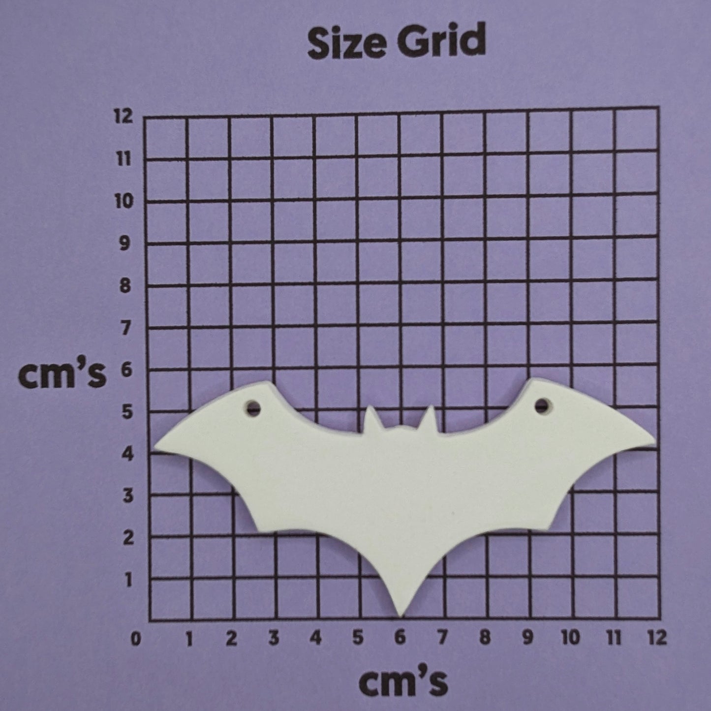 white air dried clay decoration in the shape of a bat with a hanging hole in each wind to hang it up, shown on cm size grid