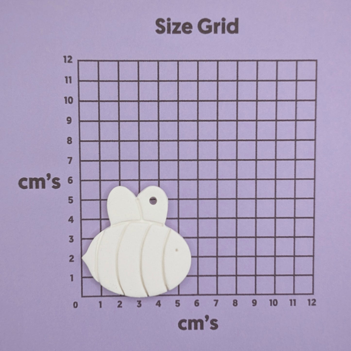 White bee-shaped decoration on a size grid with centimeter measurements on a purple background