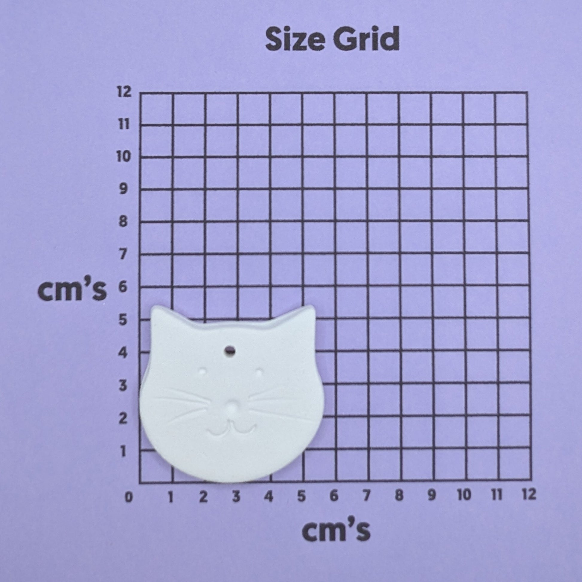 clay small cat face decoration on a size grid with measurements in centimeters 