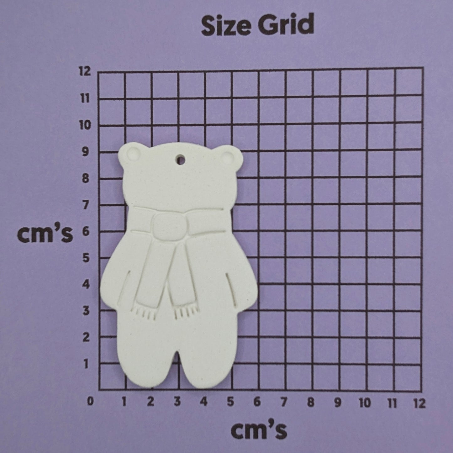 white air dried clay teddy bear ornament with a scarf stamped on, on a purple size grid in cm's