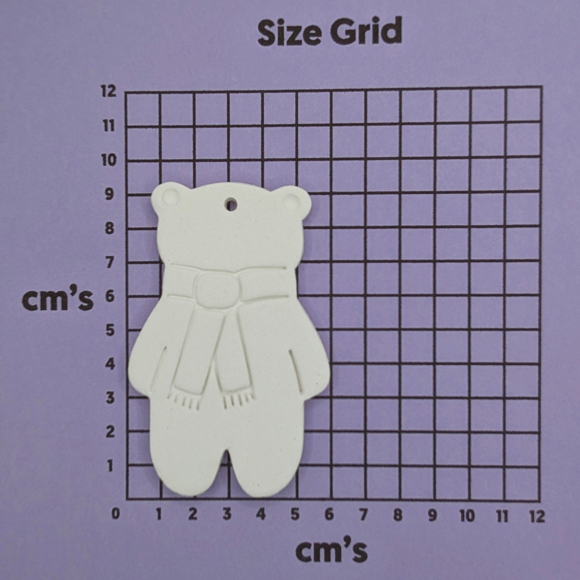 white air dried clay teddy bear ornament with a scarf stamped on, on a purple size grid in cm's