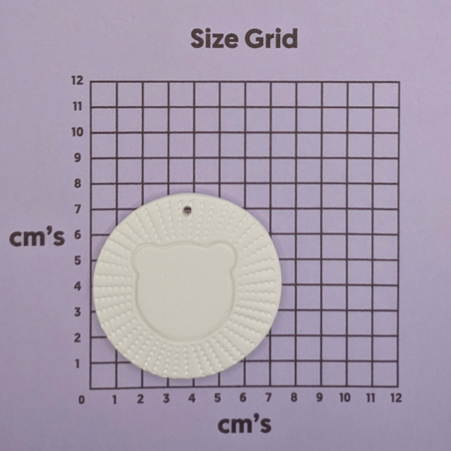 air died clay decoration in the style of a stylised lion head on a size grid with centimeter measurements.