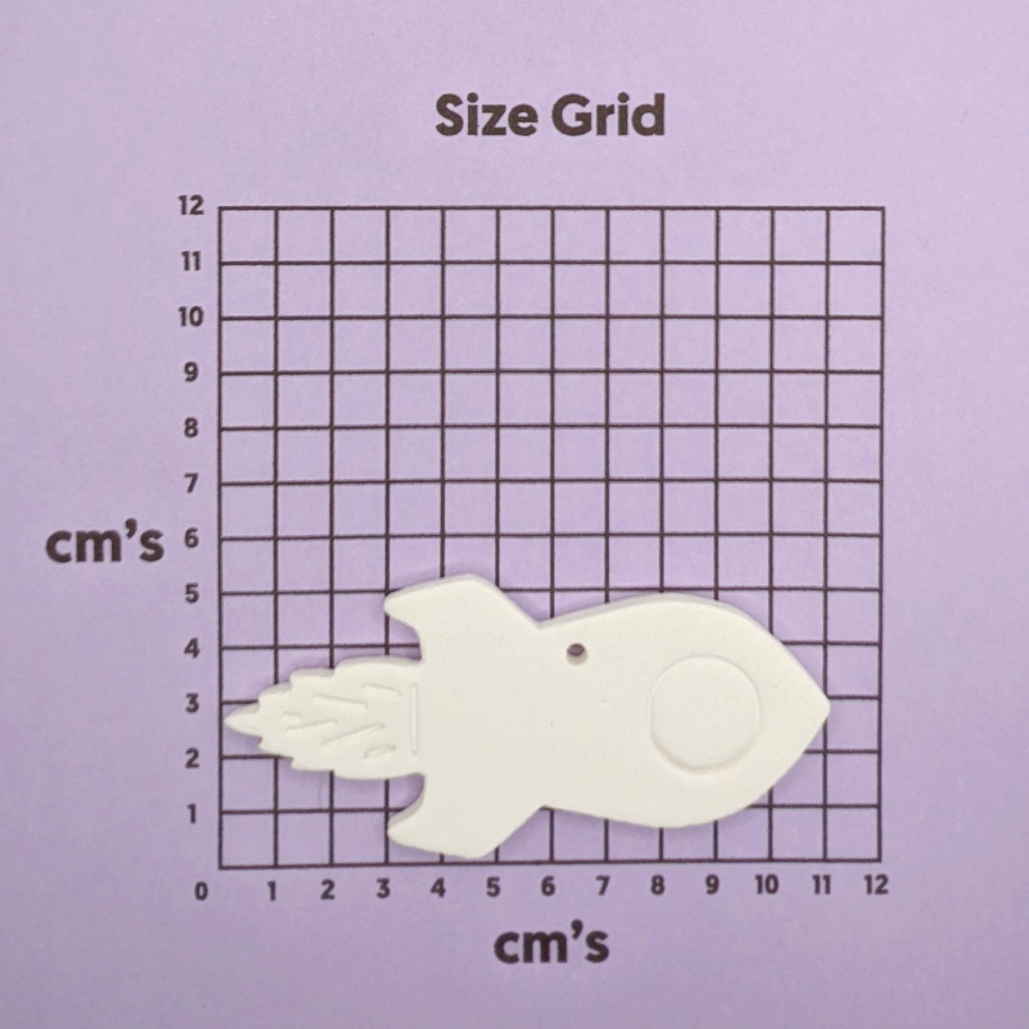 White  clay rocket shaped object on a size grid with centimeter markings on a purple background