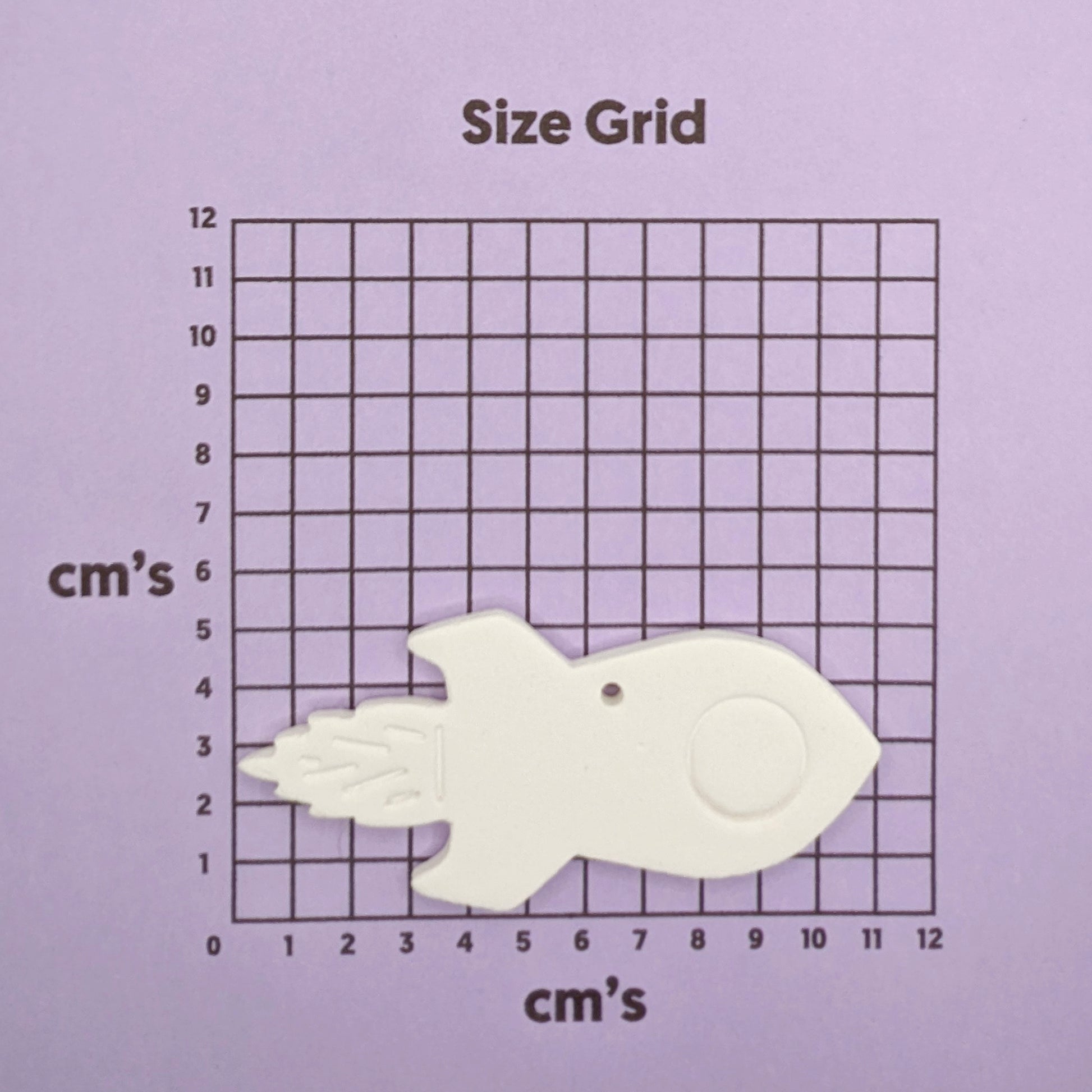 White  clay rocket shaped object on a size grid with centimeter markings on a purple background