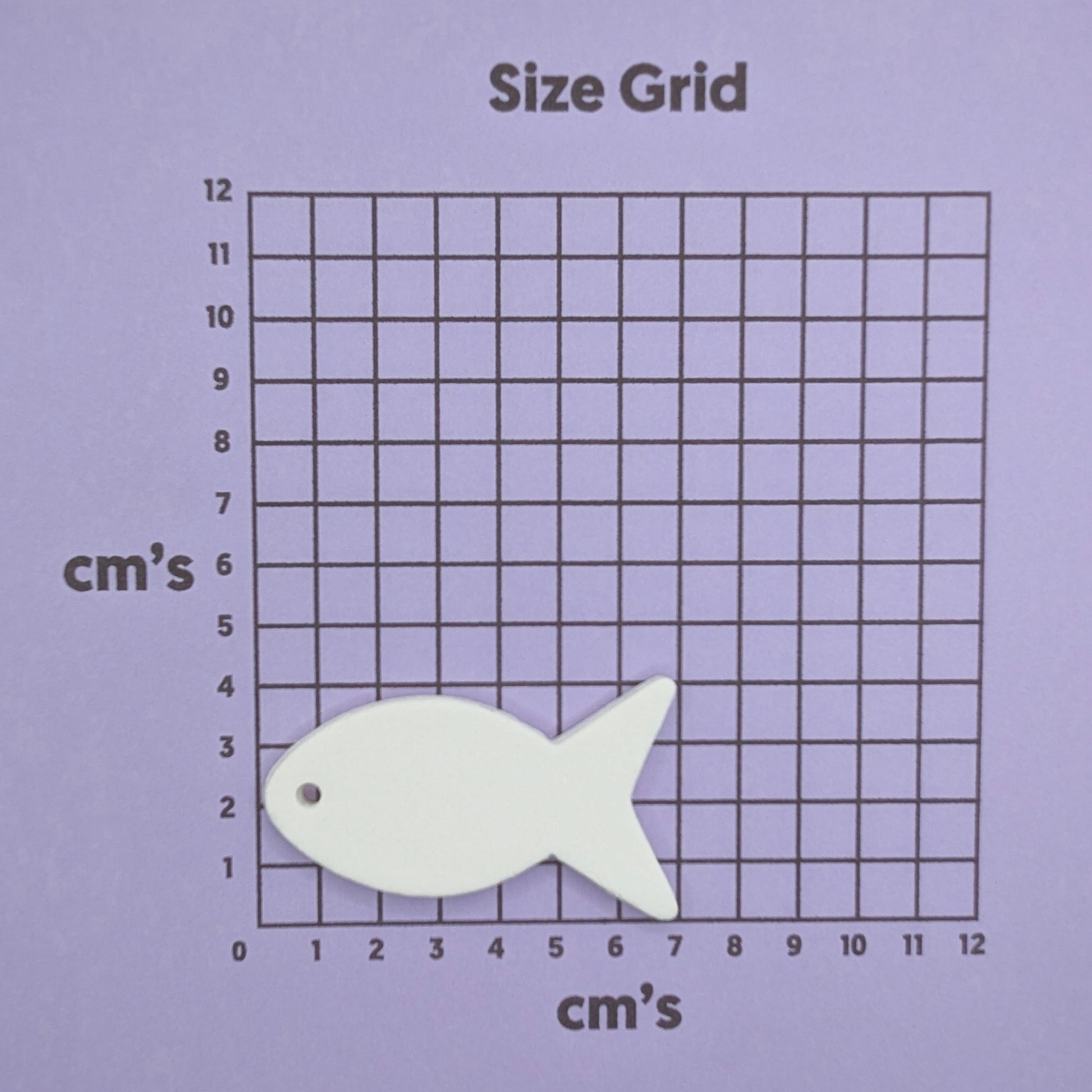 White fish-shaped clay decoration on a size grid with centimeter markings on a purple background