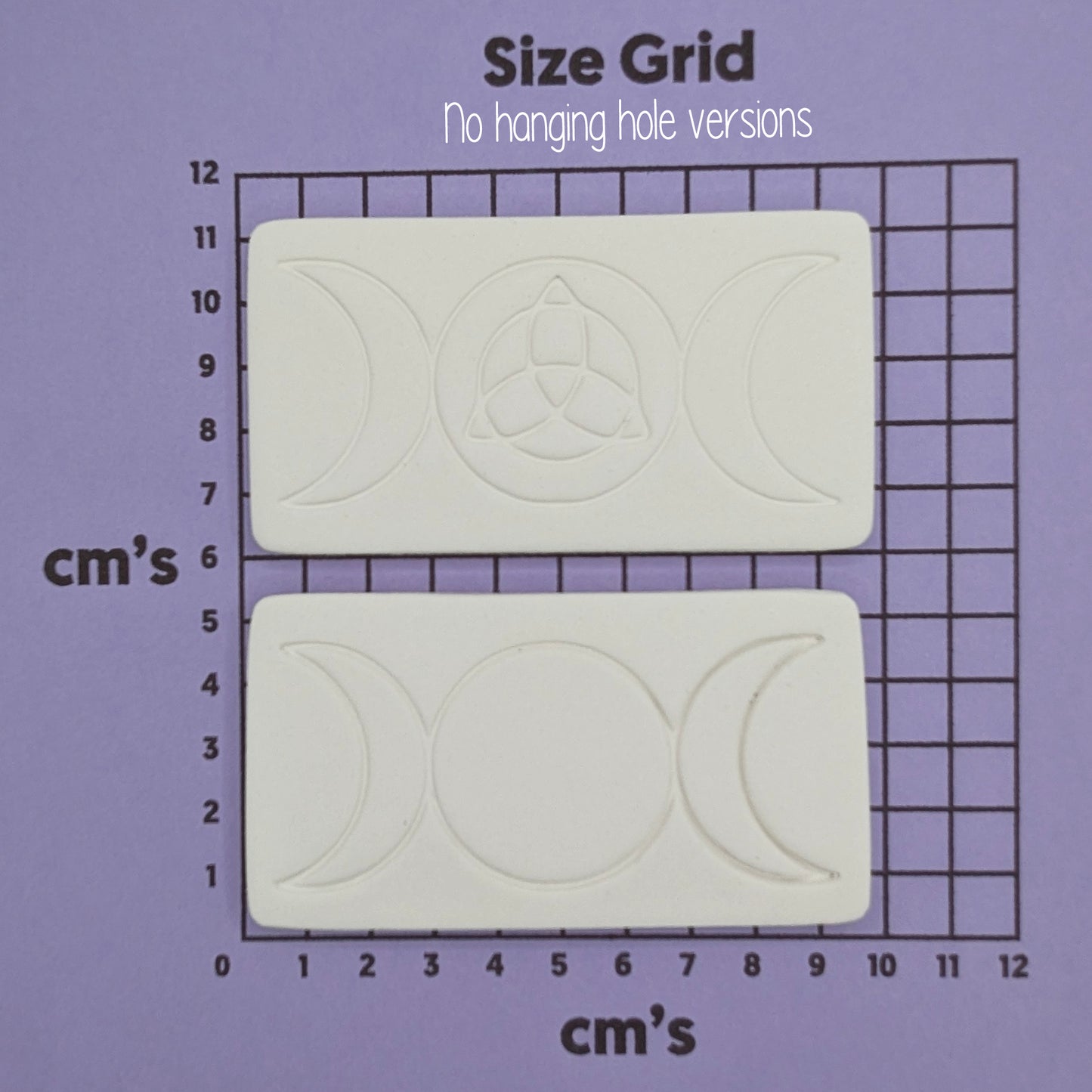 two rectangular shaped air dried clay decoration with the triple moon and triquetra symbols stamped into them shown on a purple cm size grid to show size