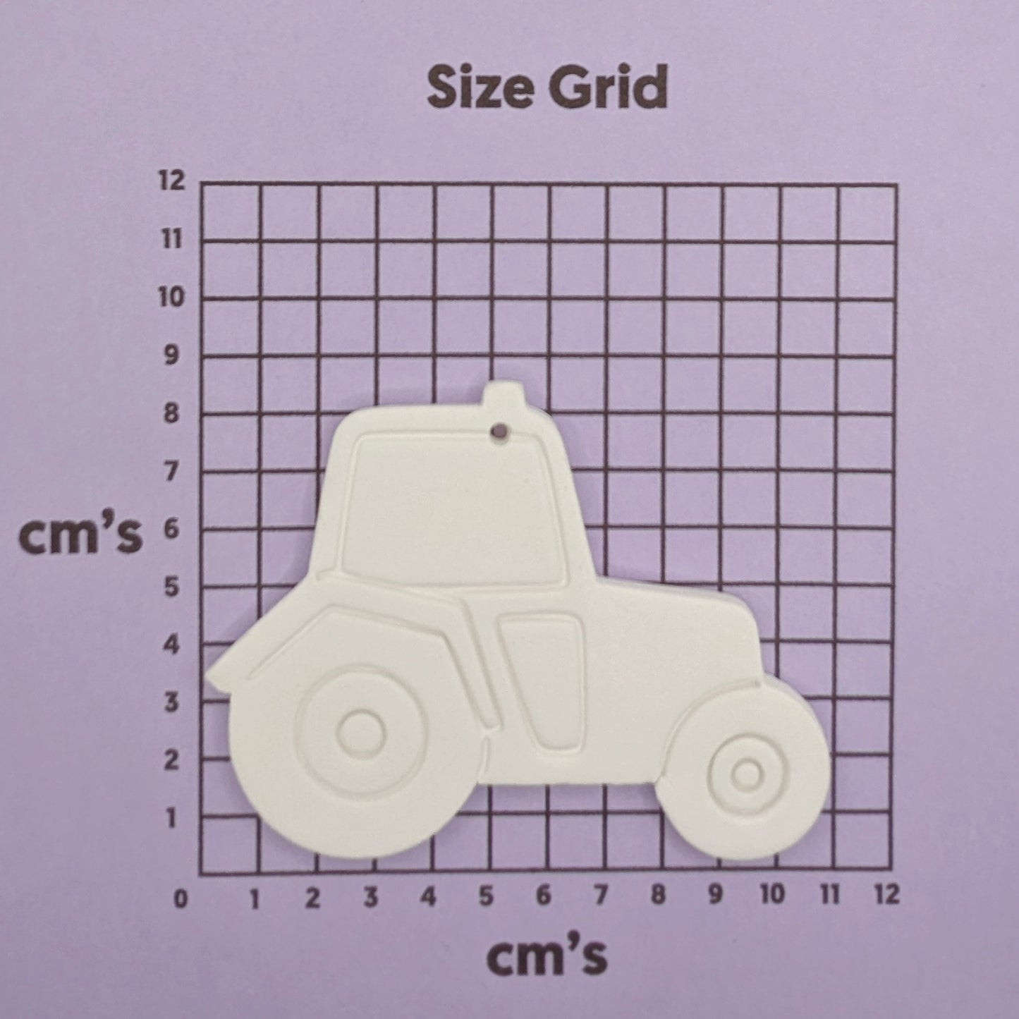 Tractor-shaped clay decoration on a size grid with measurements in centimeters.