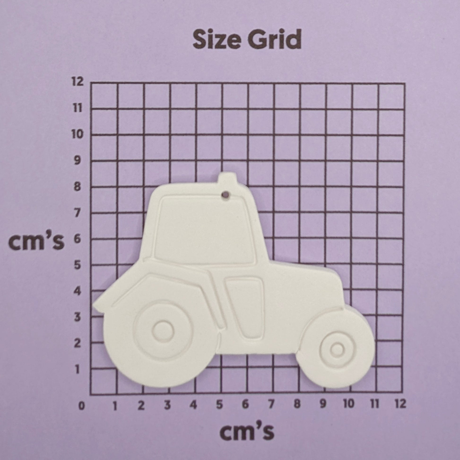 Tractor-shaped clay decoration on a size grid with measurements in centimeters.