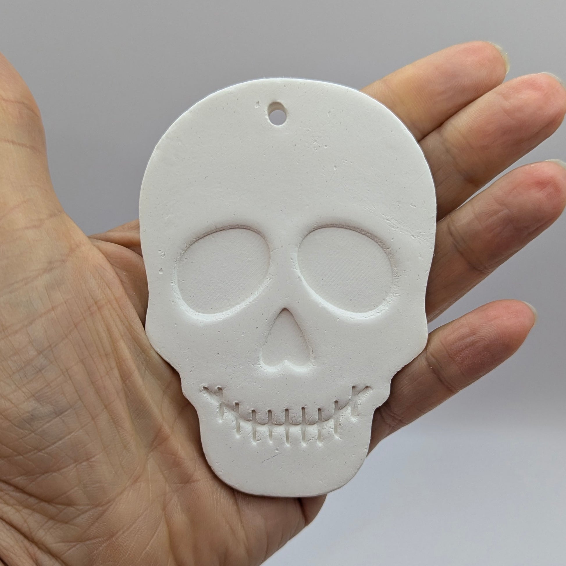 White skull-shaped clay decoration held in a hand to give scale