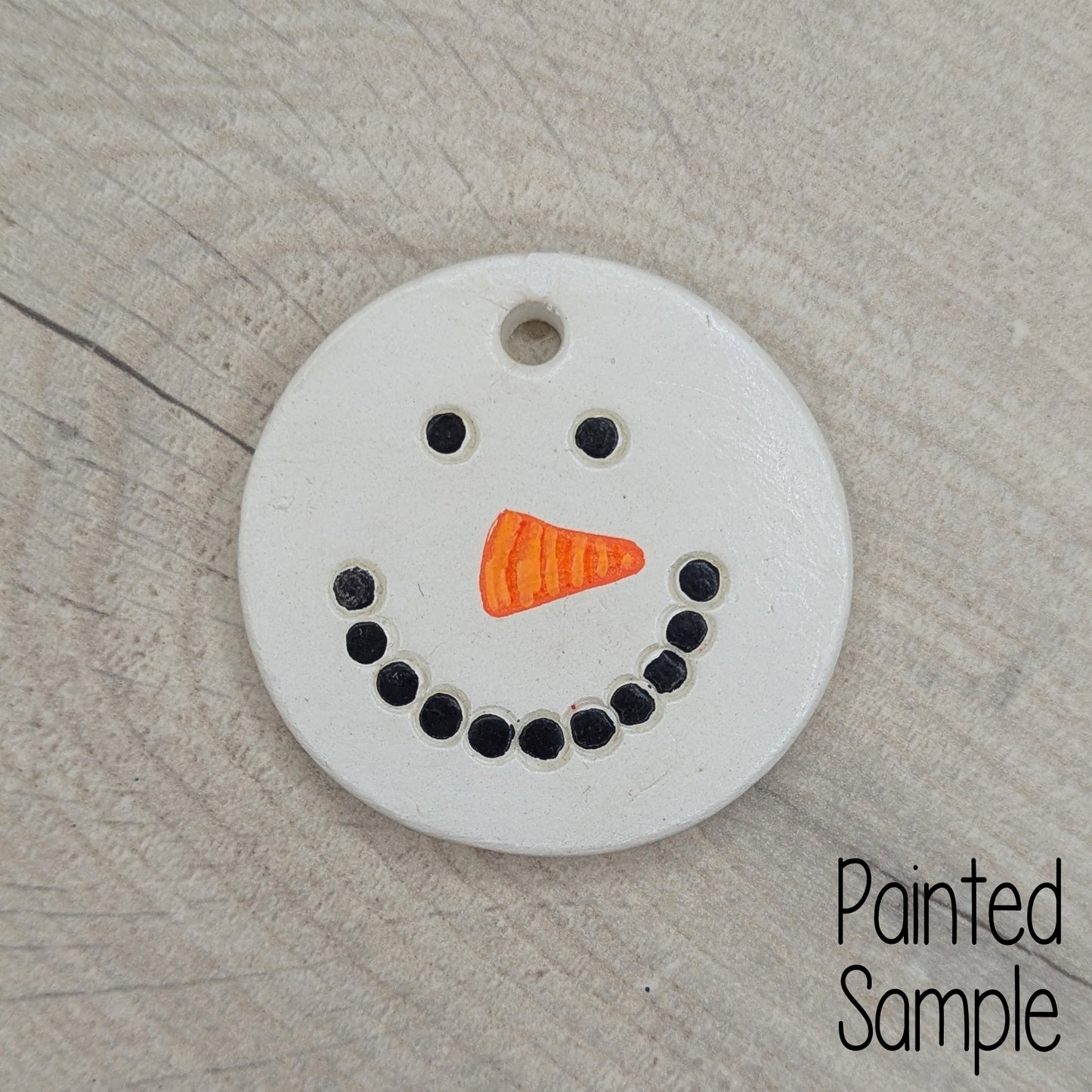 painted snowman face on clay decoration, black for coal mouth and eyes and orange triangle for carrot nose