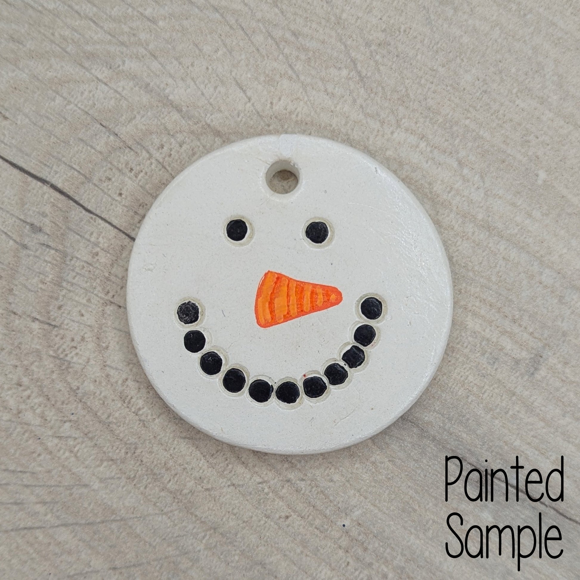 painted snowman face on clay decoration, black for coal mouth and eyes and orange triangle for carrot nose